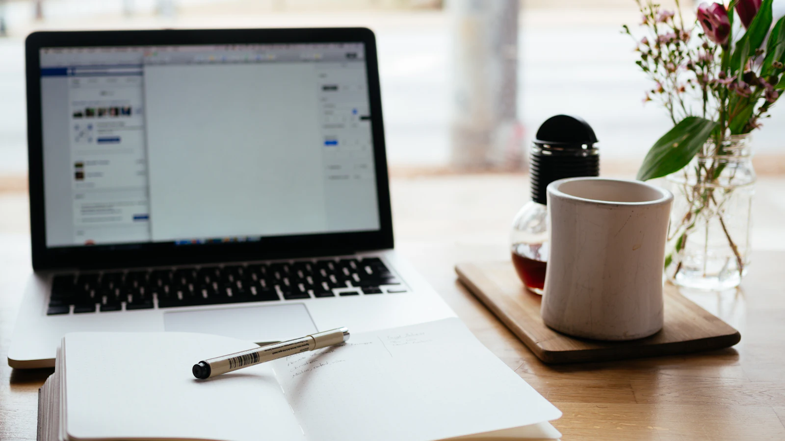 A laptop, notebook and coffee mug on a desk